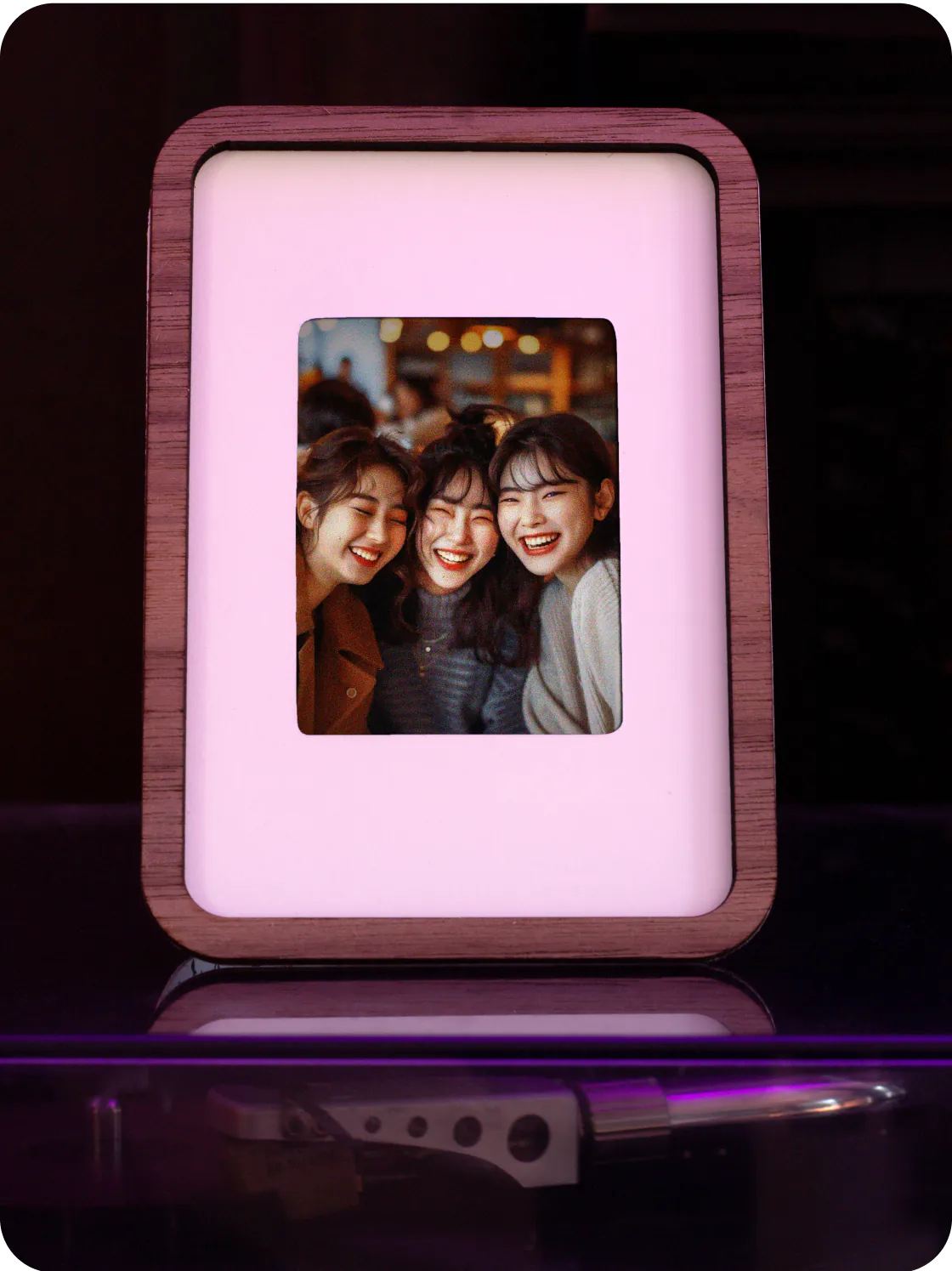 A walnut Pop-up Frame with a photo of three smiling friends, lit in pink