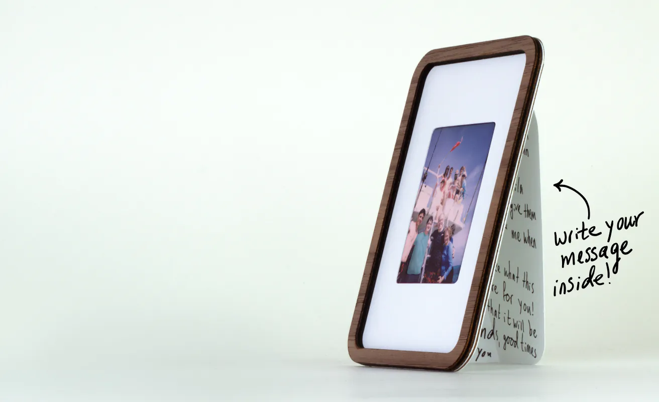 An Angl Pop-up Frame standing on a table with an Instax Mini photo inside and a handwritten note on the fold-out card that says “write your message inside!”
