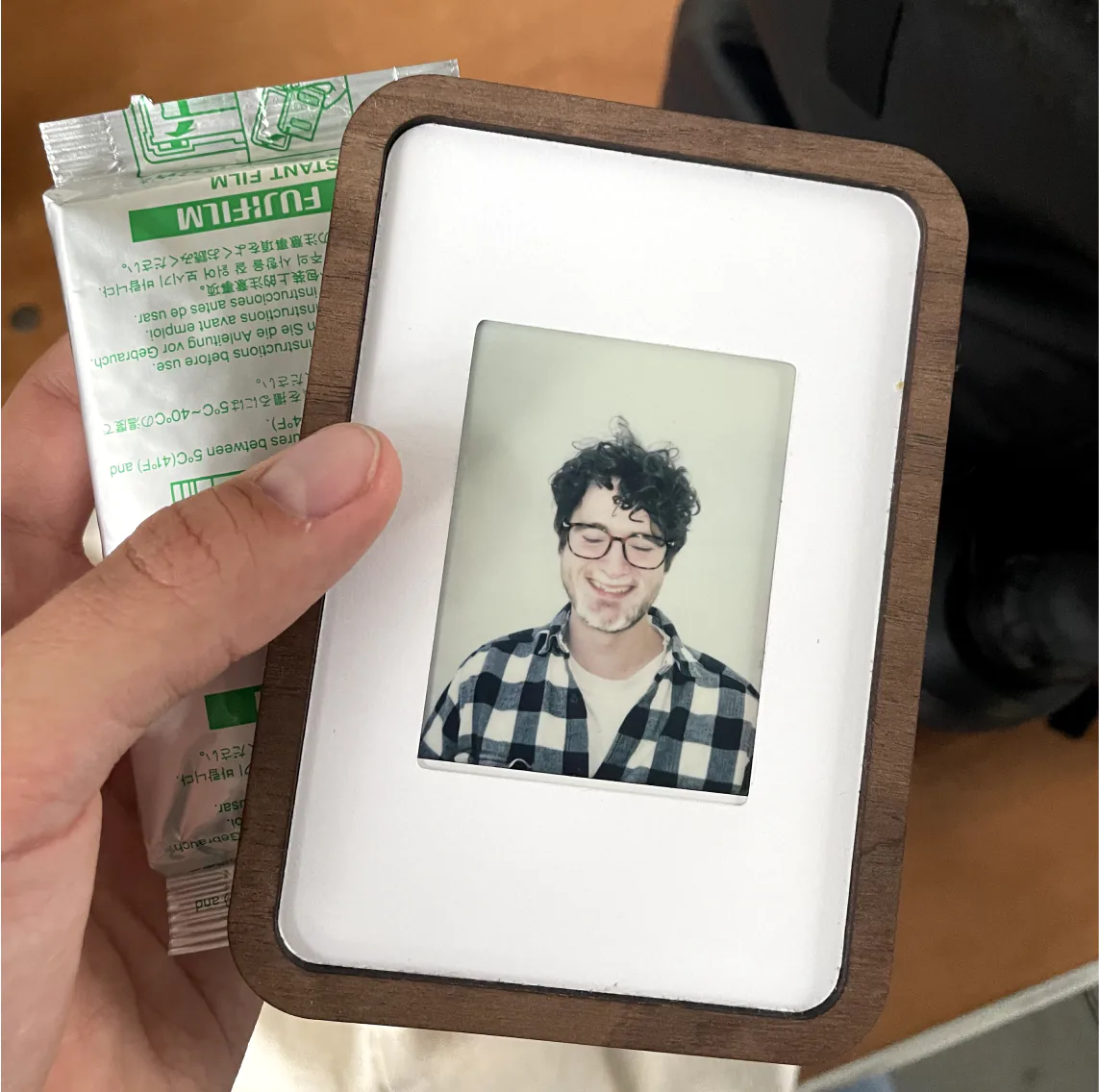 Hand holding a Pop-up Frame with an Instax portrait, next to a pack of film